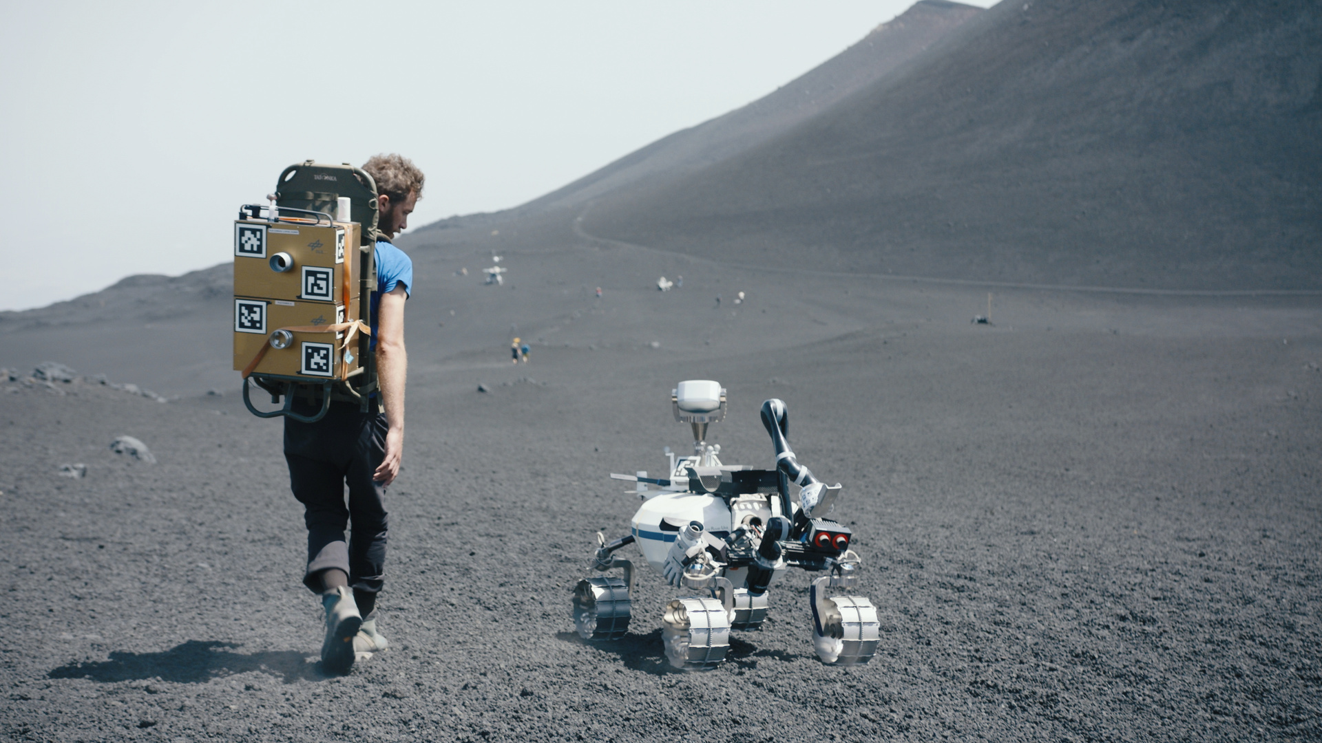 Ein Forscher des DLR spaziert mit einem Rover über die karge Landschaft des Vulkans Ätna ©  ZDF und Mattias Meinl